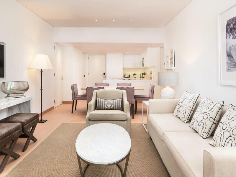 Helles Wohnzimmer mit beige Sofa, runden Tischen, Fernseher und Essbereich im Hintergrund.