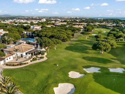 Zielone pole golfowe z piaskownicami i budynkami w tle pod niebieskim niebem.