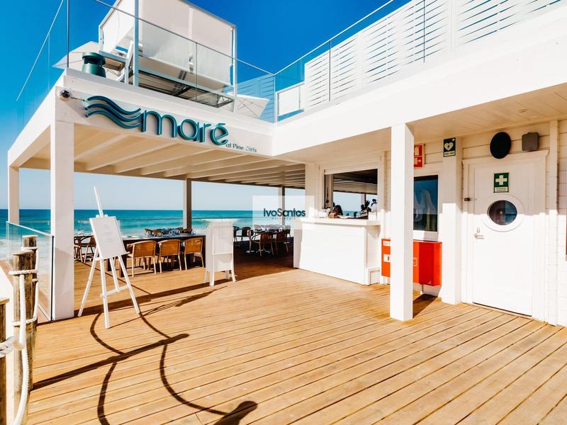 Helle Terrasse mit Holzfußboden, Bar, hohen Stühlen und Blick auf das blaue Meer.