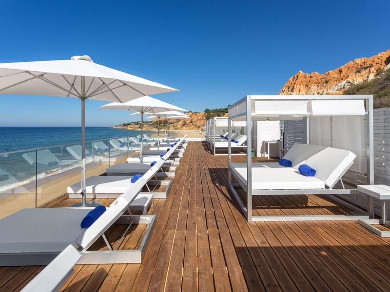 Moderner Strandbereich mit weißen Liegen, Sonnenschirmen und Holzsteg am blauen Meer.