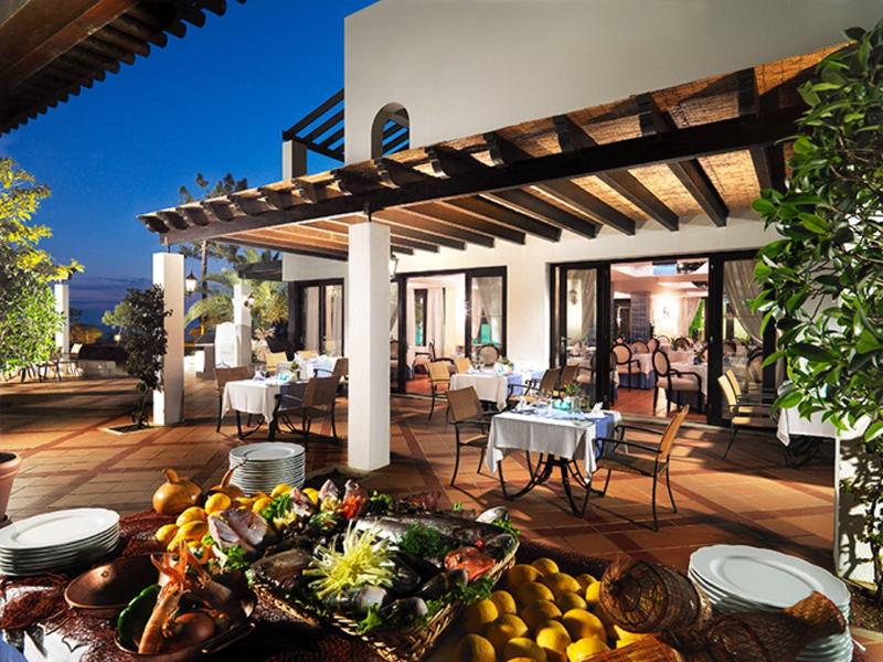 Gemütliche Terrasse mit Holzdach, gedeckten Tischen und Blumendeko bei Abenddämmerung.