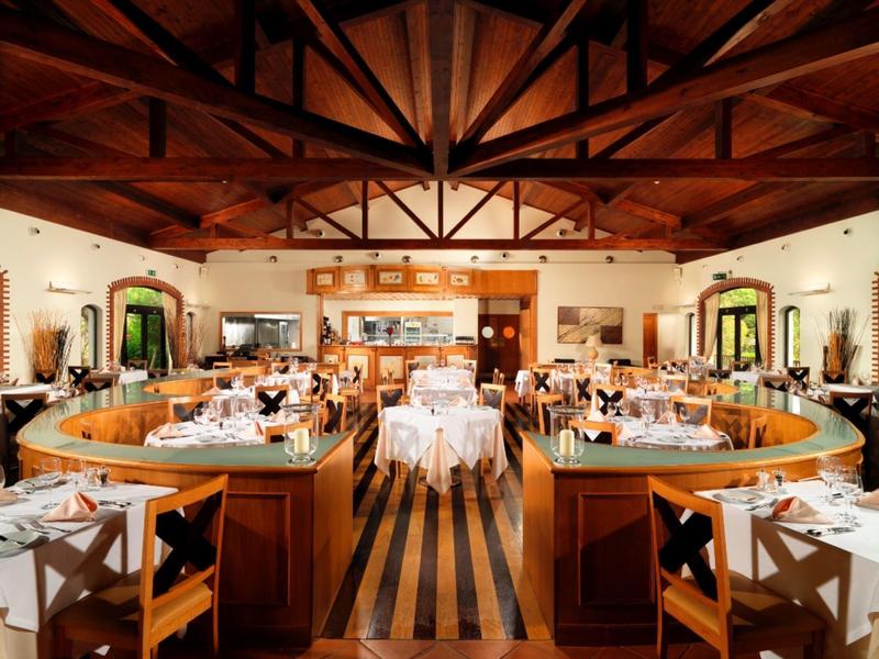 Elegantes Restaurant mit Holzdecke, runden Tischen und weiß gedeckten Tafeln in warmem Licht.