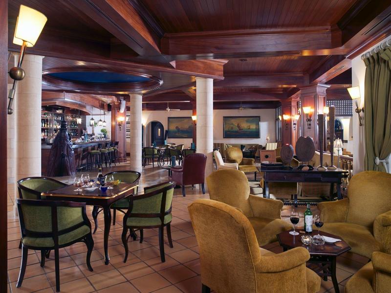 Gemütlicher Hotelbarraum mit warmem Holzdekor, runden Tischen, Sesseln und gedämpfter Beleuchtung.