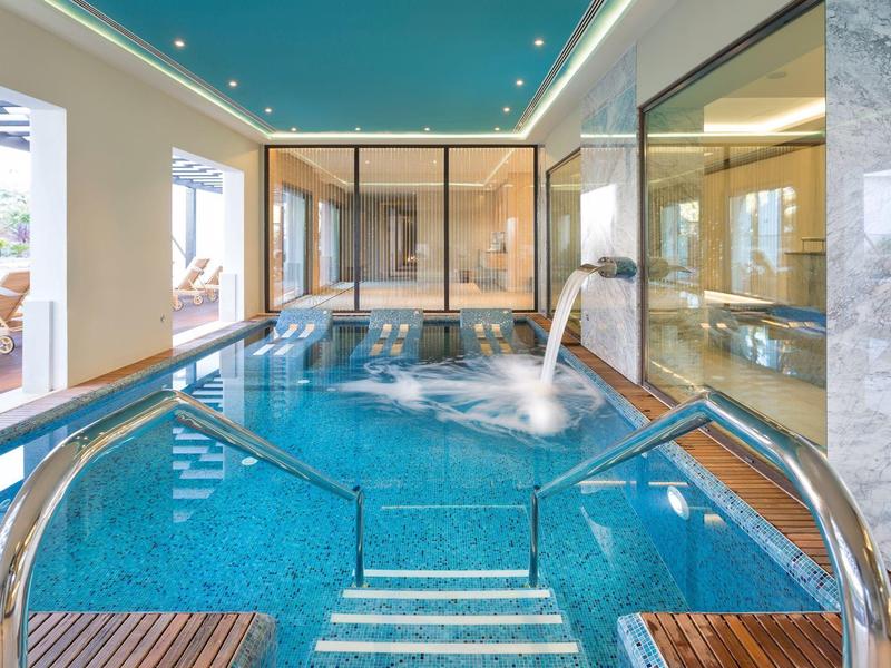 Innenpoolbereich mit Wasserfallfunktion und moderner Beleuchtung an der Decke.