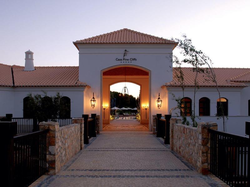 Stilvolles Gebäude mit rotem Dach und großer Durchgangsöffnung, umgeben von Mauern und Bäumen.