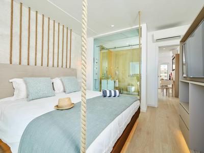 Helles Schlafzimmer mit modernem Bett, Holzvertäfelung und Glaswand zur Badezimmerecke.