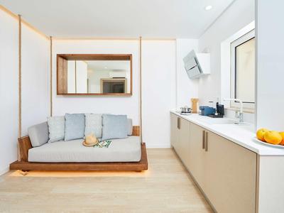 Modern, lichte hotelkamer met witte bank, houten accenten en kitchenette met fruit.