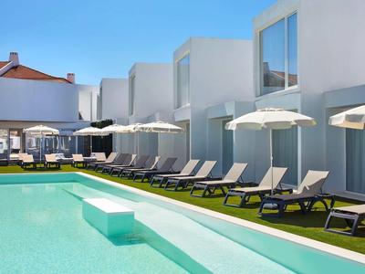 Moderner Pool mit Liegestühlen und weißen Sonnenschirmen unter klarem blauem Himmel.