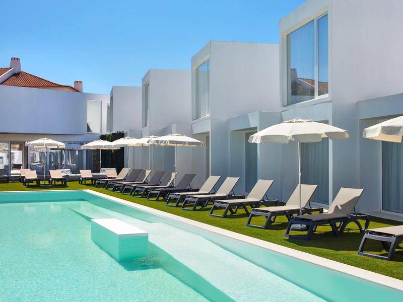 Moderner Pool mit Liegestühlen und weißen Sonnenschirmen unter klarem blauem Himmel.