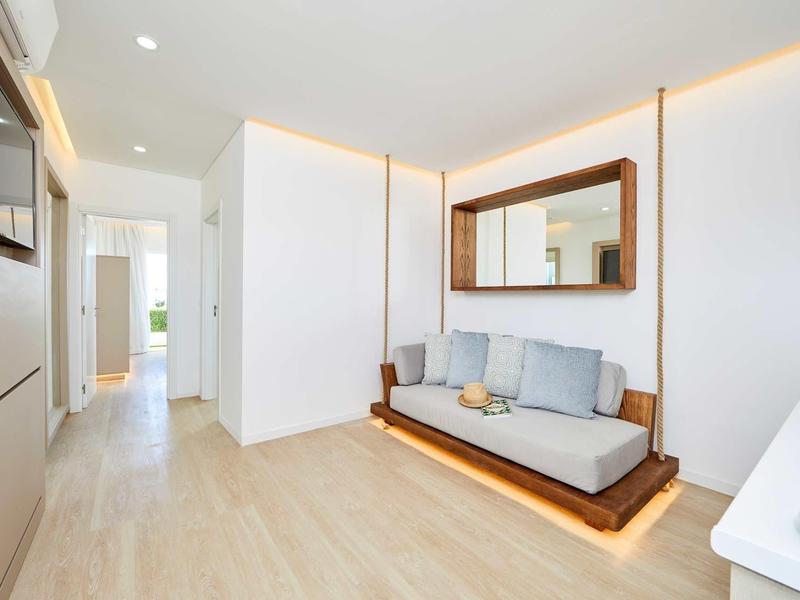 Helles, modernes Wohnzimmer mit Holzboden, grauem Sofa, großem Spiegel und indirekter Beleuchtung.