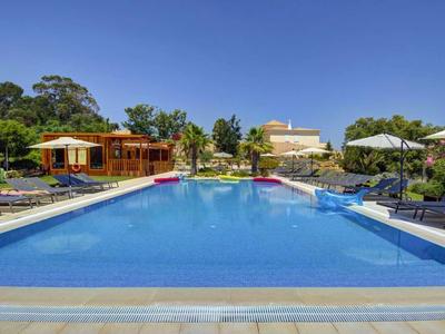 Ein großer Außenpool mit Liegestühlen und einem Gebäude im Hintergrund unter klarem Himmel.