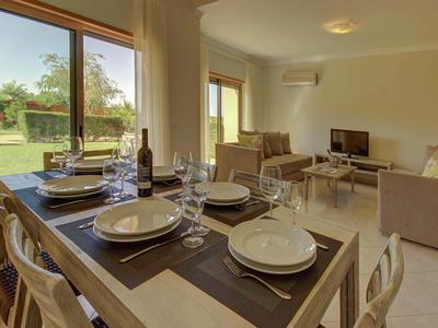 Essbereich mit gedecktem Tisch und Wohnzimmer mit Sofas und Fernseher in einem hellen Raum.