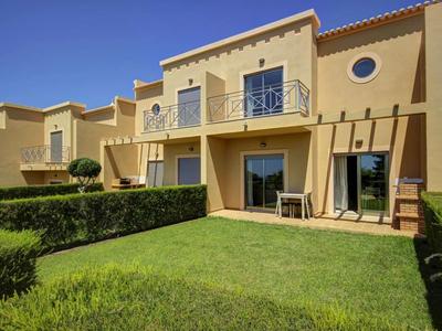 Gelbes zweistöckiges Ferienhaus mit Terrasse, Balkon und grünem Rasen im Vordergrund.