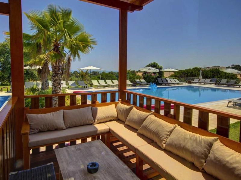 Gezellig terras met sofa en uitzicht op het zwembad onder een heldere blauwe lucht.