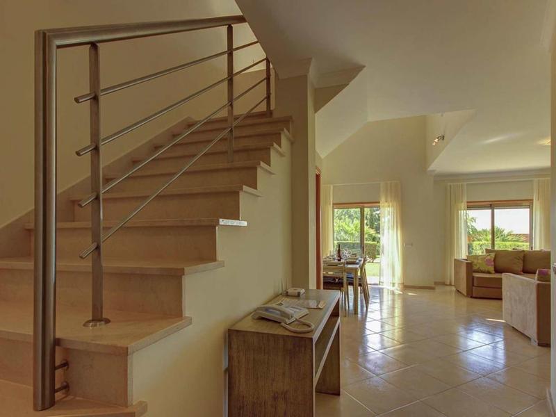 Lichte binnenruimte met trap, betegelde vloer en uitzicht naar buiten door grote ramen.