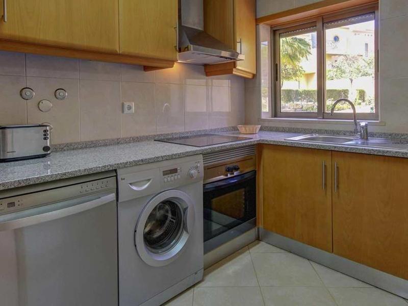 Moderne keukenhoek met wasmachine, vaatwasser, oven en raam met uitzicht op buiten.