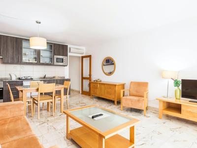 Lichte woonkamer met kitchenette, eettafel, fauteuils en tv in moderne stijl.