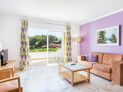 Lichte woonkamer met paarse muur, bruine bank, houten meubels en uitzicht op terras met tuin.