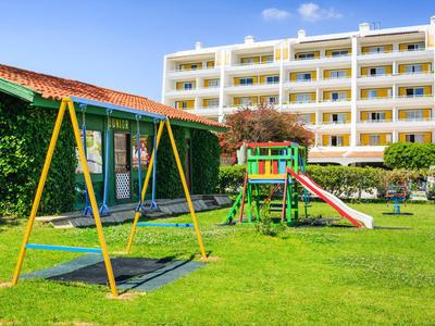 Een goed onderhouden speeltuin met schommels en glijbaan voor een meerlaagse hotelgebouw.