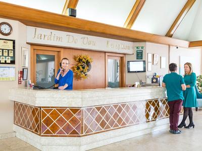 Helle Hotelrezeption mit freundlichem Personal und zwei Gästen, warme Holzakzente und Pflanzen.