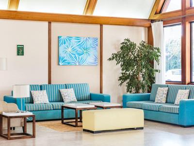 Heller, moderner Hotellobby-Bereich mit türkisfarbenen Sofas, Pflanzen und Kunst an der Wand.