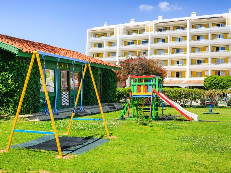 Een goed onderhouden speeltuin met schommels en glijbaan voor een meerlaagse hotelgebouw.