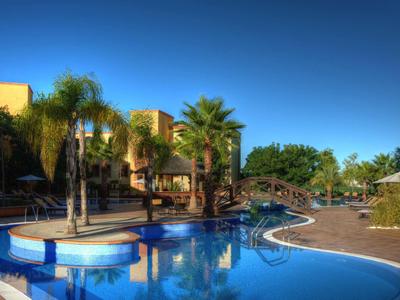 Ein blauer Pool mit Palmen, Sonnenschirmen und einem klaren Himmel im Hintergrund.
