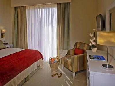 Gemütliches Hotelzimmer mit großem Bett, roter Tagesdecke, Sessel und Schreibtisch mit Lampe.