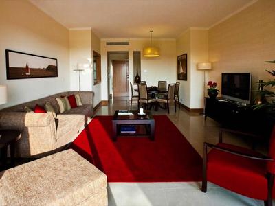 Gemütliches Wohnzimmer mit rotem Teppich, Sofas und einem Fernseher in einer Hotel-Suite.