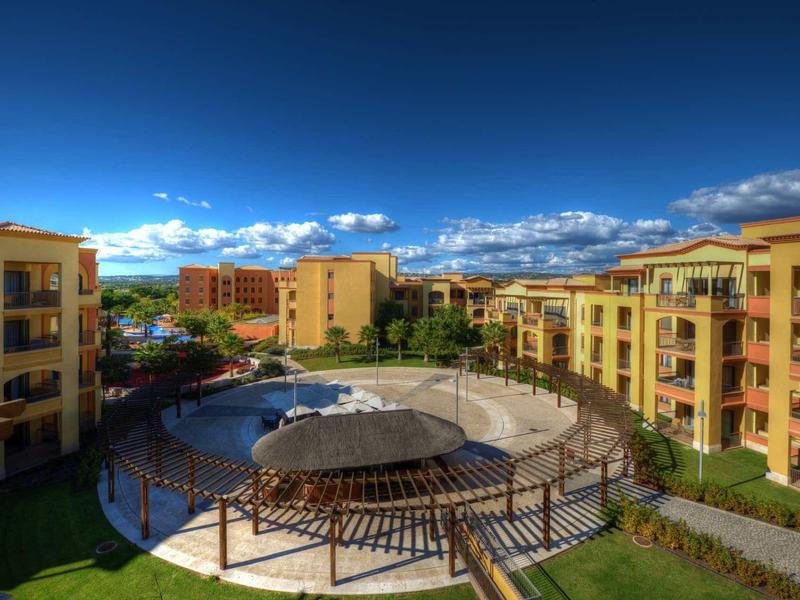 Vue d'une piscine d'hôtel entourée de bâtiments jaunes sous un ciel bleu clair.