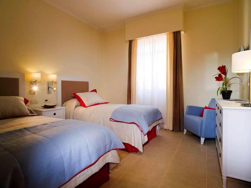 Chambre d'hôtel confortable avec deux lits simples, chaise, bureau et éclairage chaleureux.