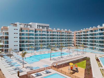 Moderner Hotelkomplex mit mehreren Swimmingpools, Sonnenliegen und Palmen unter klarem Himmel.