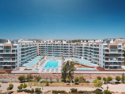 Große moderne Hotelanlage mit zwei Pools und umliegenden Apartments unter blauem Himmel.