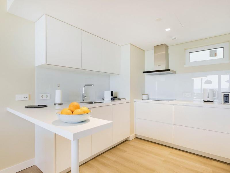 Moderne, helle Küche mit weißen Schränken, Holzfußboden und einfacher, klarer Gestaltung.