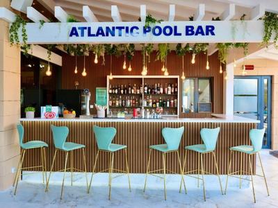 Moderní pool bar s tyrkysovými barovými židličkami a dekorativními rostlinami.