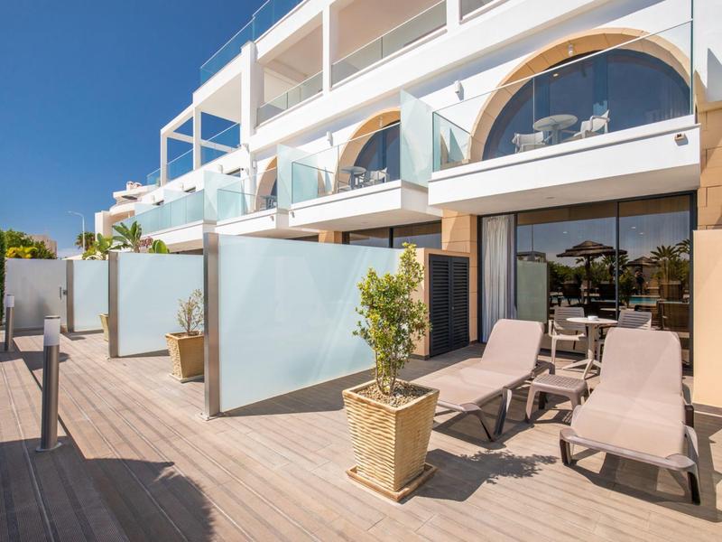 Terrace with sun loungers and plants in front of hotel rooms under blue sky