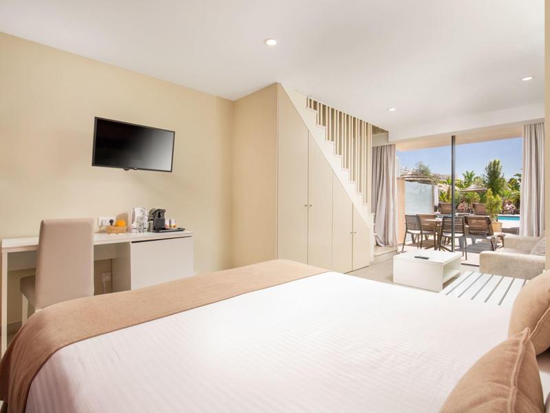 Modern hotel room with bed, desk, TV, and balcony with seating area.