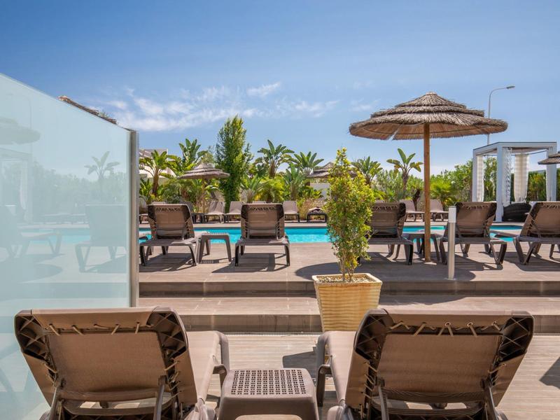 Sun terrace with lounge chairs, plants, and umbrellas beside a hotel pool.
