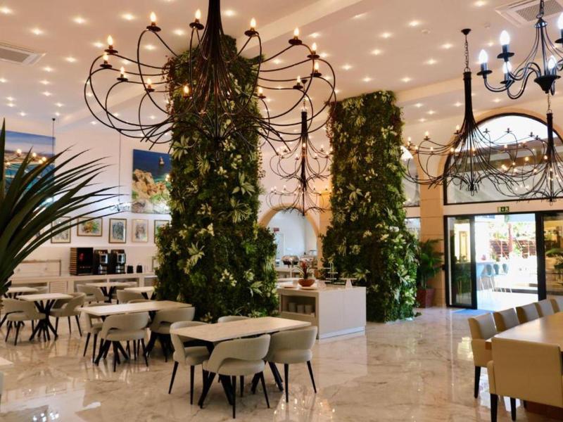 Bright, modern restaurant with green wall plants and elegant chandeliers.