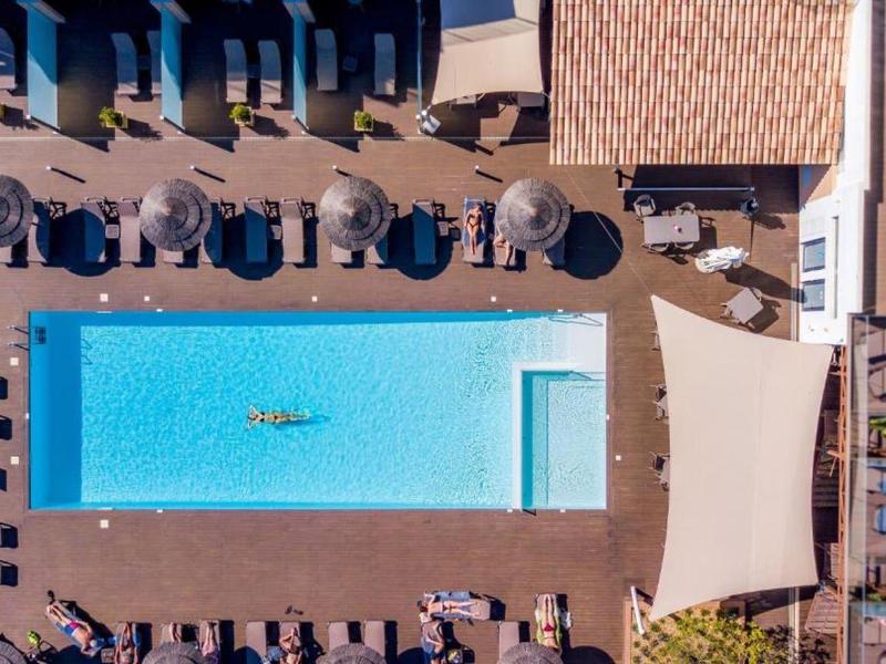 Drone view of a rectangular pool surrounded by lounge chairs and umbrellas.