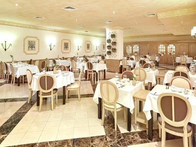 Jasna restauracja z okrągłymi stołami, białymi obrusami i beżowymi krzesłami w eleganckim stylu.