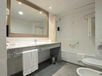 Jasna łazienka z dużym lustrem, wanną, toaletami i nowoczesnym wyposażeniem.