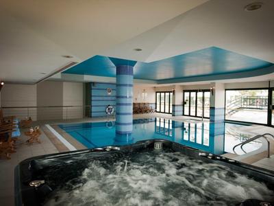 Wnętrze hotelu z basenem i jacuzzi, dużo naturalnego światła przez duże okna.