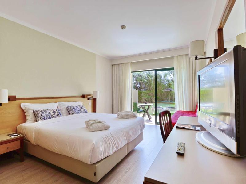 Lichte hotelkamer met tweepersoonsbed, terras en uitzicht op de natuur.