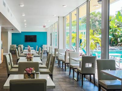 Hell eingerichteter Sitzbereich mit großen Fenstern, Tischgruppen und hellgrauen Polsterstühlen.