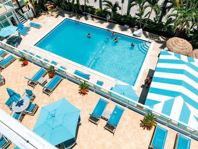 Großes blaues Schwimmbad mit Liegestühlen, Sonnenschirmen und Palmen, sommerliche Atmosphäre.