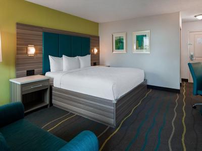 Modernes Hotelzimmer mit großem Bett, grünem Akzentwand, Schreibtisch und gemütlichem Sessel.