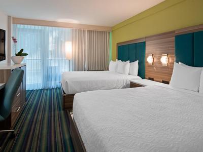 Modernes Hotelzimmer mit zwei großen Betten, blau-grünen Kopfteilpaneelen und gestreiftem Teppichboden.