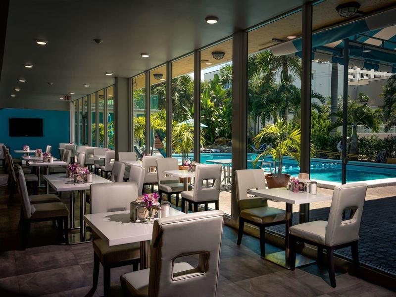 Moderner Restaurantbereich mit weißen Stühlen und Tischen neben einem Pool und großen Glasfenstern.