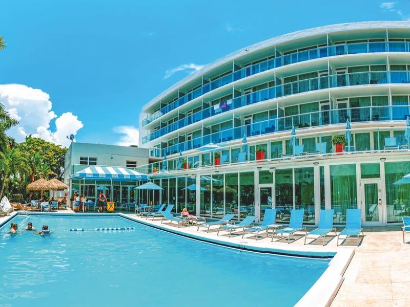 Moderner Hotelkomplex mit großem Pool, Sonnenliegen, Palmen und klarem blauem Himmel.